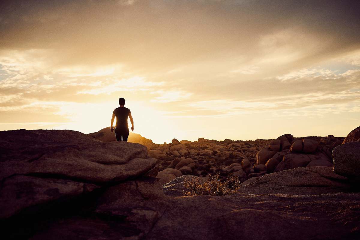 rock man walking on gray rocks under yellow sky during daytime sunrise